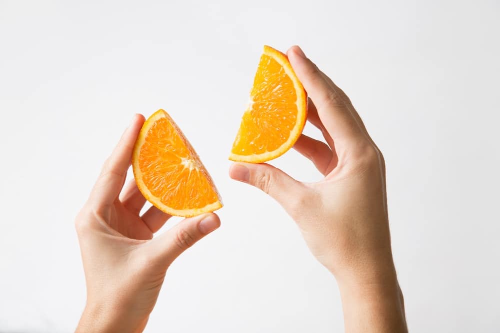 Human hands holding cut orange sections